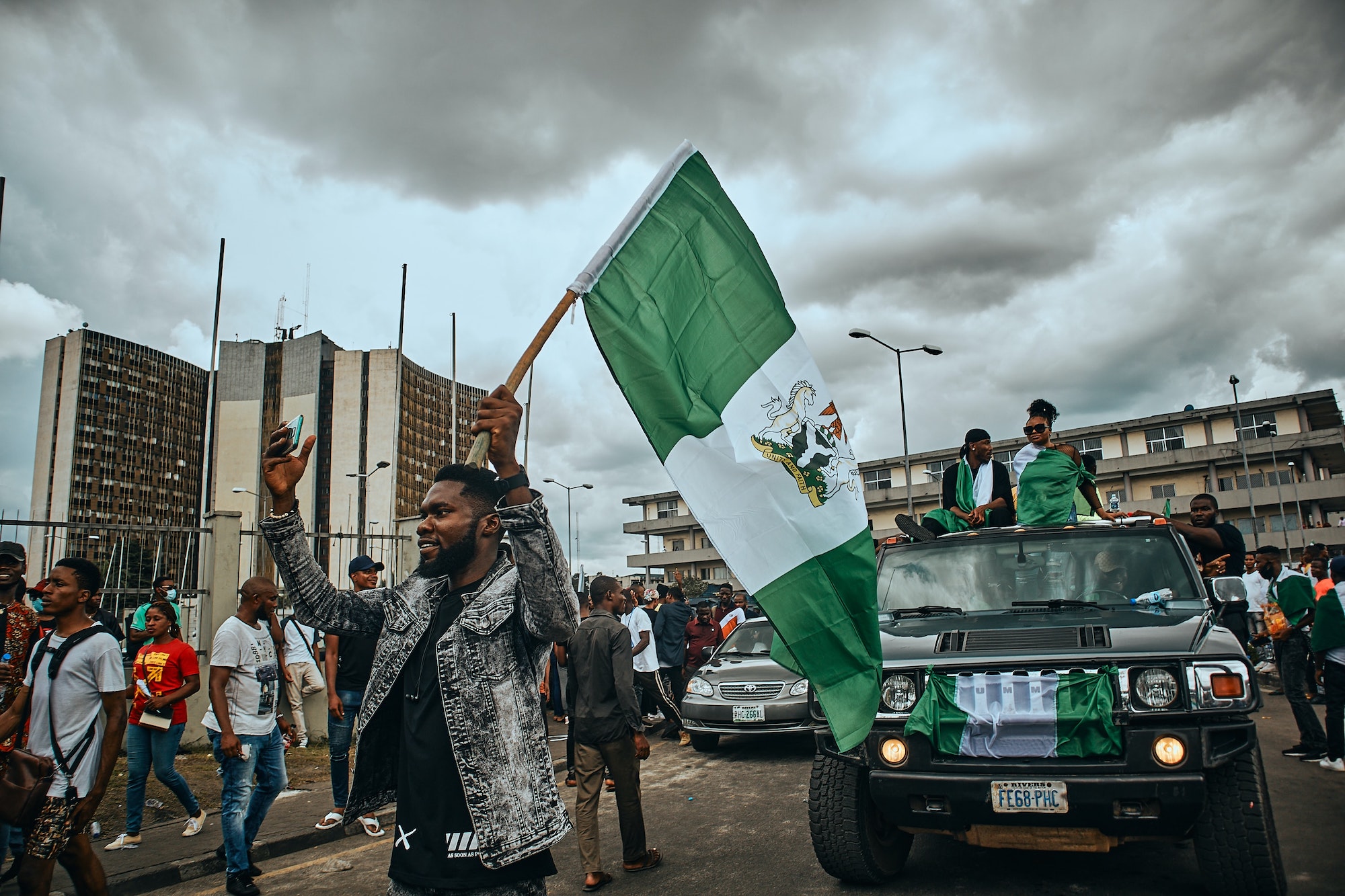 Protestors on foot and in cars holding the Nigerian flag. Photo by Emmanuel Ikwuegbu on Unsplash.