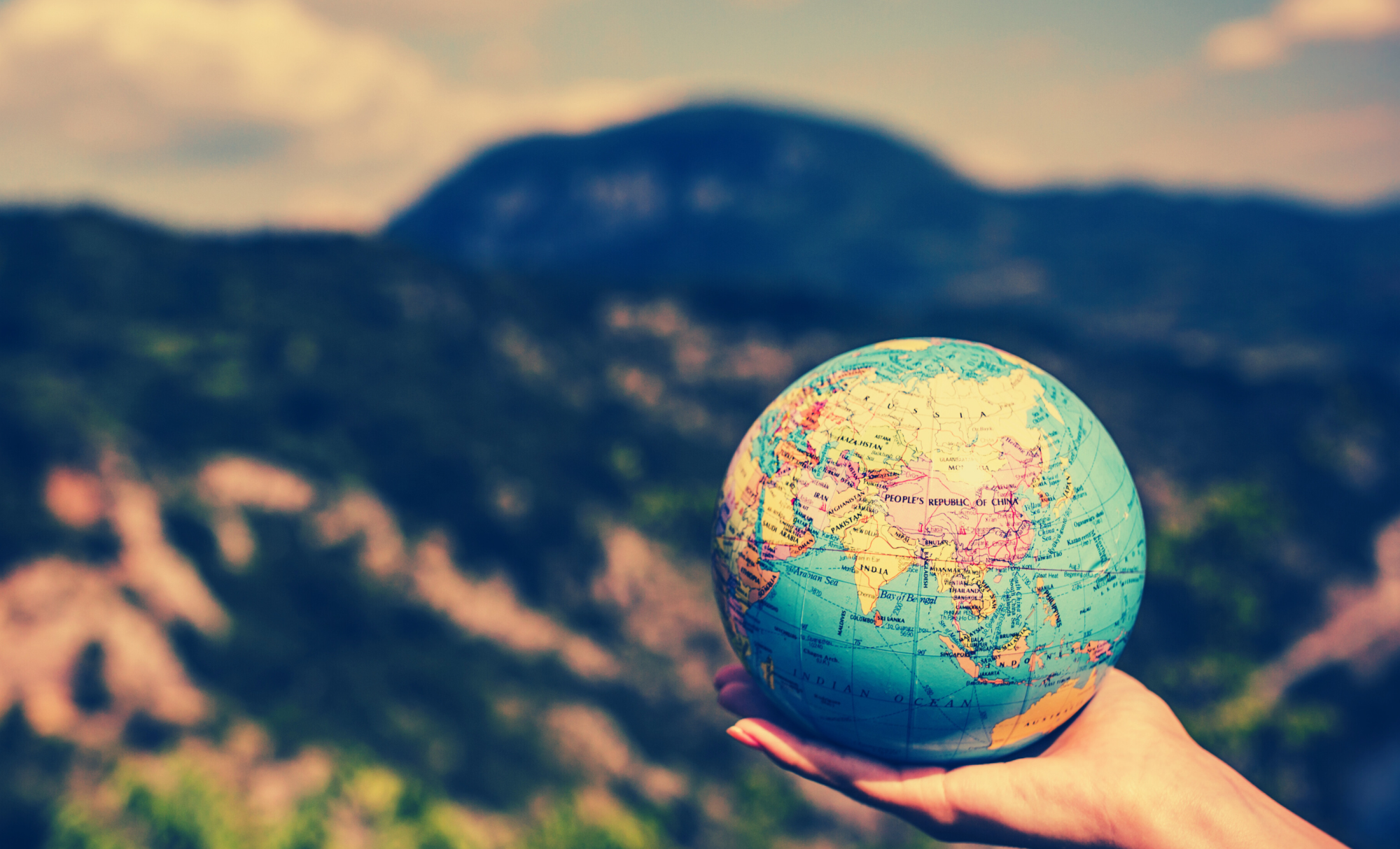 Globe held in hand against backdrop of mountains