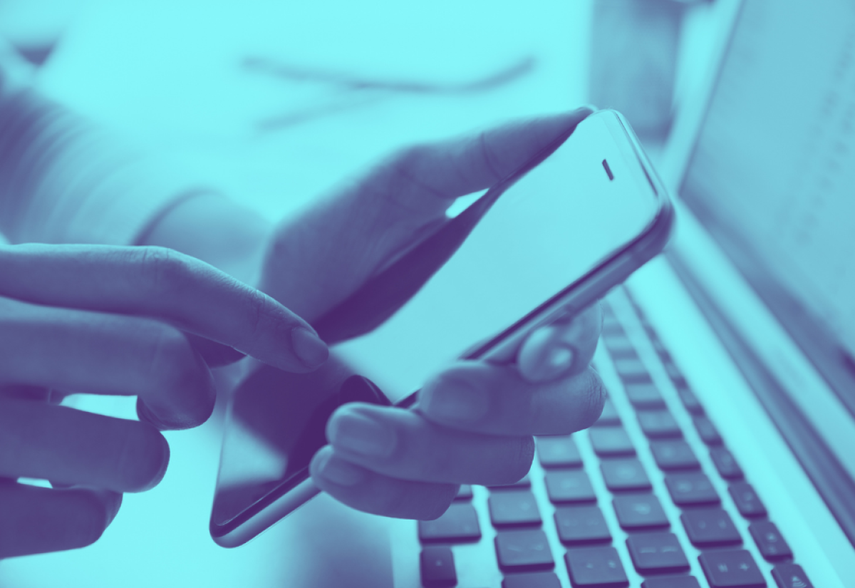 Close-up on hands holding smartphone above computer keyboard